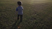 A young, cute happy boy in a blue shirt running in sunrise or sunset sunlight in green grass in cinematic slow motion.