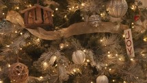 Wooden nativity, Joy, and other ornaments on a Christmas tree with gold ribbon and lights