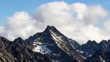 A dominant rocky peak in a high alpine landscape. Fluffy clouds over the rocks .Zoom out