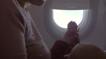 Woman holding a baby while it plays with a toy on an airplane.