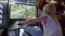 Girl with blonde ponytail plays a motorcycle racing game at an arcade, focused on the screen