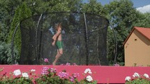 A young teenager leaps on a trampoline amidst blooming garden flowers