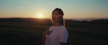 Slomo shot of a woman making the sign of the cross in a field during sunset