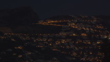 Small night city on a hill in Spain - the glowing lights of houses create dark patches of trees against the dark blue night sky