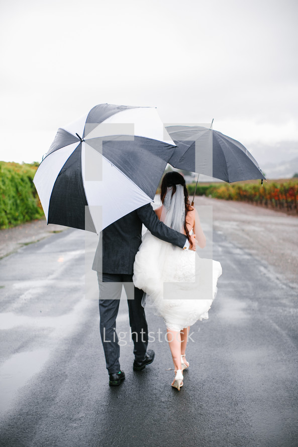 bride and groom walking carrying umbrellas 