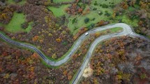 Top view of a winding road with a white van driving among autumn-colored trees