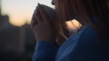 Woman drinking a mug of hot beverage at sunrise