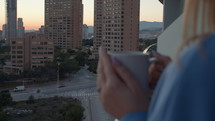 Woman drinking a warm beverage on a balcony in the city