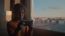 Boy sitting by a window playing games on his phone