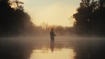 Young fly fisherman casting on a foggy river at sunrise