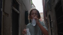 Slow motion - a teenager wanders the narrow streets of Venice, Italy. He enjoys a snack from a bag and sips water as he meanders through the historic alleys