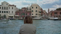 Rear view of a teenager in striped shirt observing historical buildings by the Venice canal