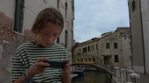 Young teen engrossed in his smartphone amidst the historic canals and architecture of Venice