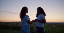 Two girls praying at dusk in a field 2