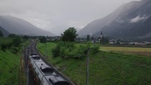 Wide shot - a train approaches in the Alps, captured from a bridge, the landscape features mountains and mist in a wide shot.