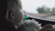 toddler in a carseat looking out a car window 