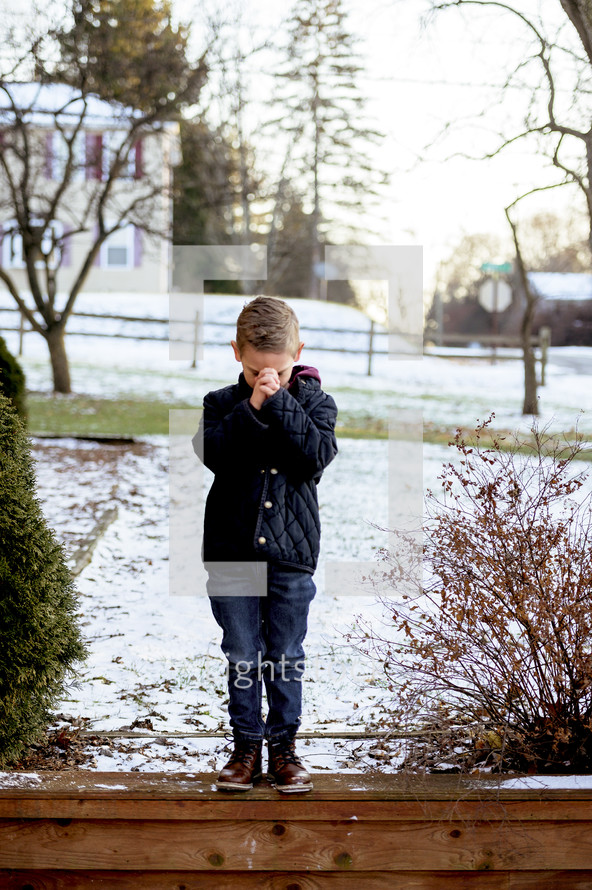 boy praying outdoors in the snow 