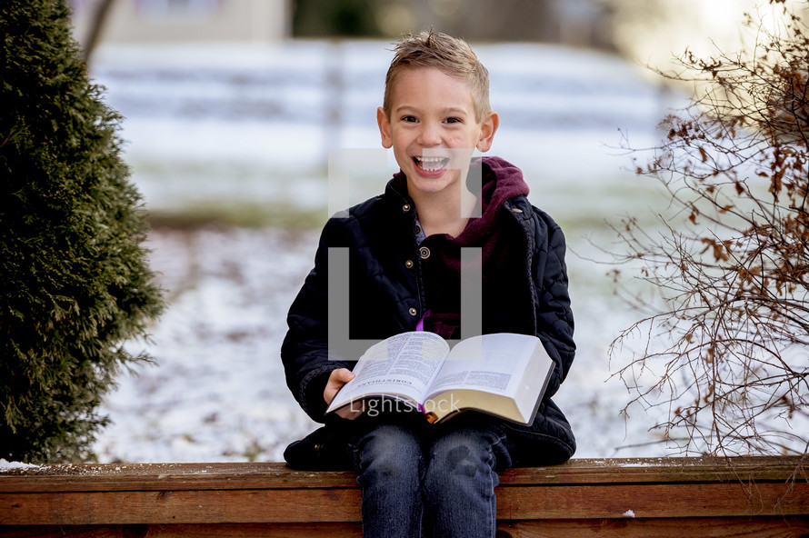 a boy reading a Bible outdoors in winter 
