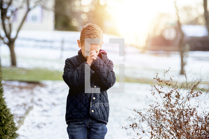 boy child praying outdoors in snow 