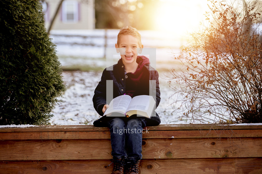 a child sitting outdoors in snow reading a Bible 
