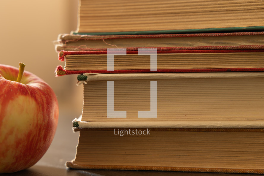 Red apple with stack of vintage books, close up