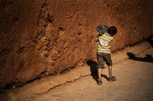 boy carrying a jug of water near a wall 