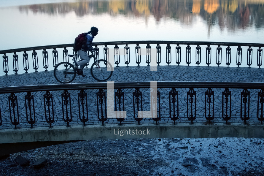 Anonymous hooded cyclist crossing a paved old bridge.
