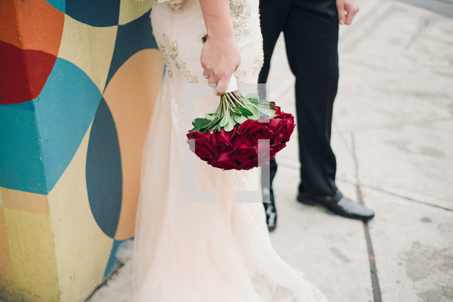 a bride holding red roses and a groom 