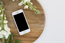 phone and white flowers on a cutting board against a white background 