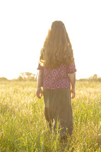 teen girl in a long skirt walking through a field of tall grasses 