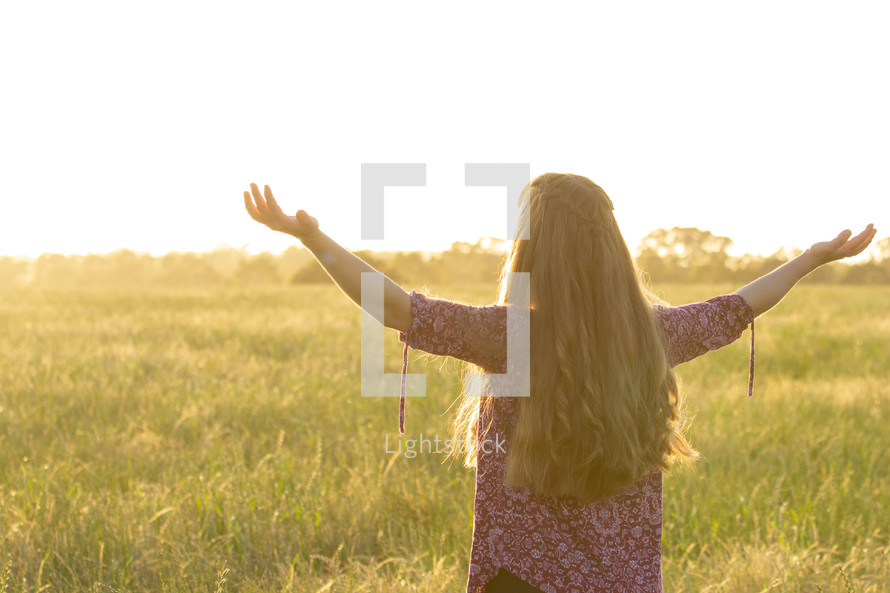 a girl with raised hands standing in a field 