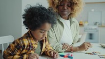 Little African AmericanBoy Drawing on Paper with Mother at Home
