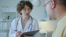 Female Doctor Interviewing Patient and Taking Notes during Consultation
