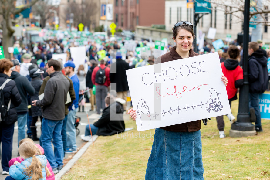 Woman holding pro-life sign at rally with crowds in background