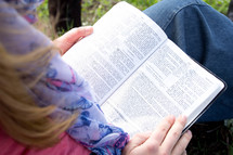 a woman reading a Bible in her lap outdoors