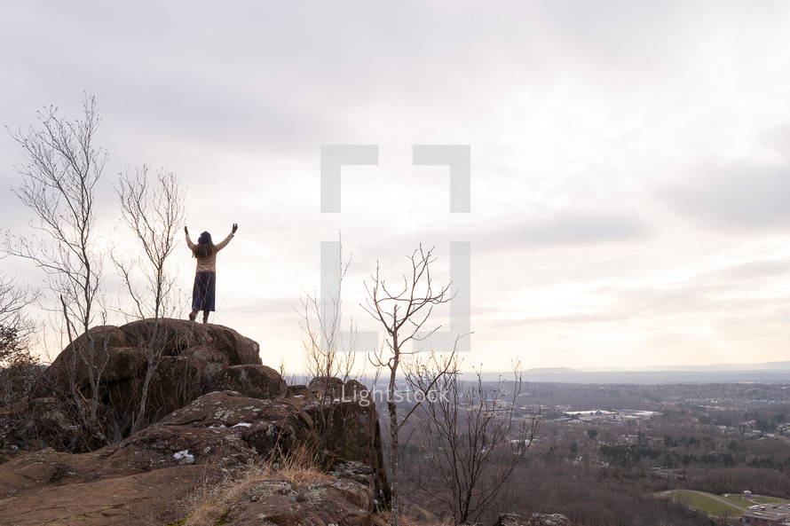 a woman standing on a mountaintop with raised hands 