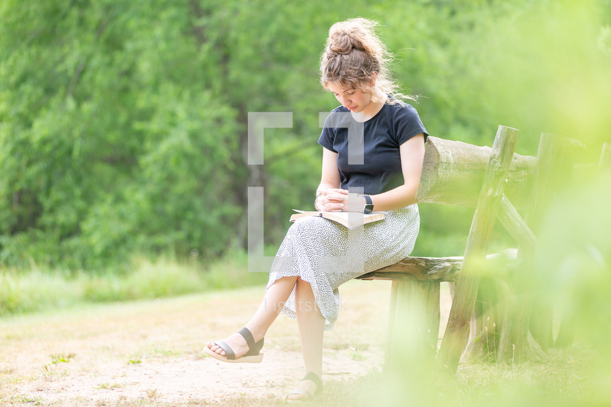 Young woman sitting on a bench reading the Bible