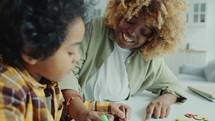 Preschool Boy Filling In Coloring Page with Help of Mom at Home
