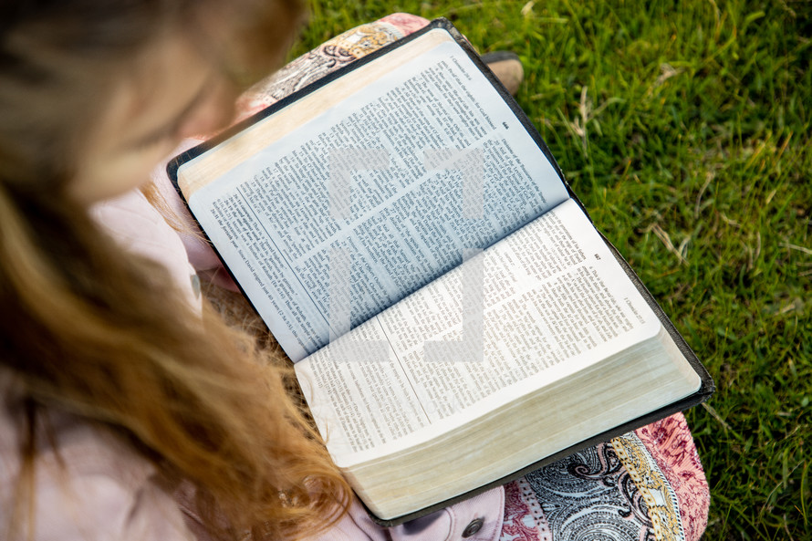 a girl sitting in a field reading a Bible 