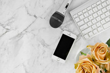 iPhone, microphone, computer keyboard, and yellow roses on a marbled background 