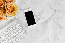 cellphone, computer keyboard, and yellow roses on a marbled background 