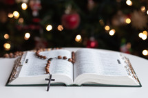 open Bible and rosary in front of a Christmas tree 