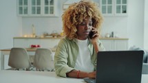 Young African American Woman Talking on Phone and Working on Laptop at Home
