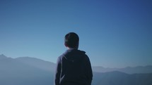 Young man looking out at mountains and raises his hands