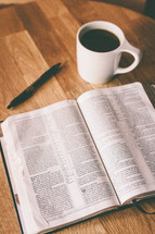 An open Bible and a cup of coffee on a table.