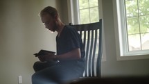 young man sitting in a chair reading a Bible 