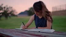 Woman Reading Bible and Journaling Outside at Sunset