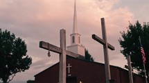 Crosses in front of a church with steeple and clouds in the sky
