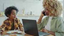 Mother Calling on Phone and Working Laptop during Breakfast with Child
