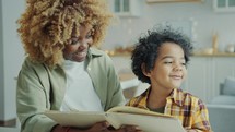 African American Mother Smiling and Reading Fairytale in Book with Little Son
